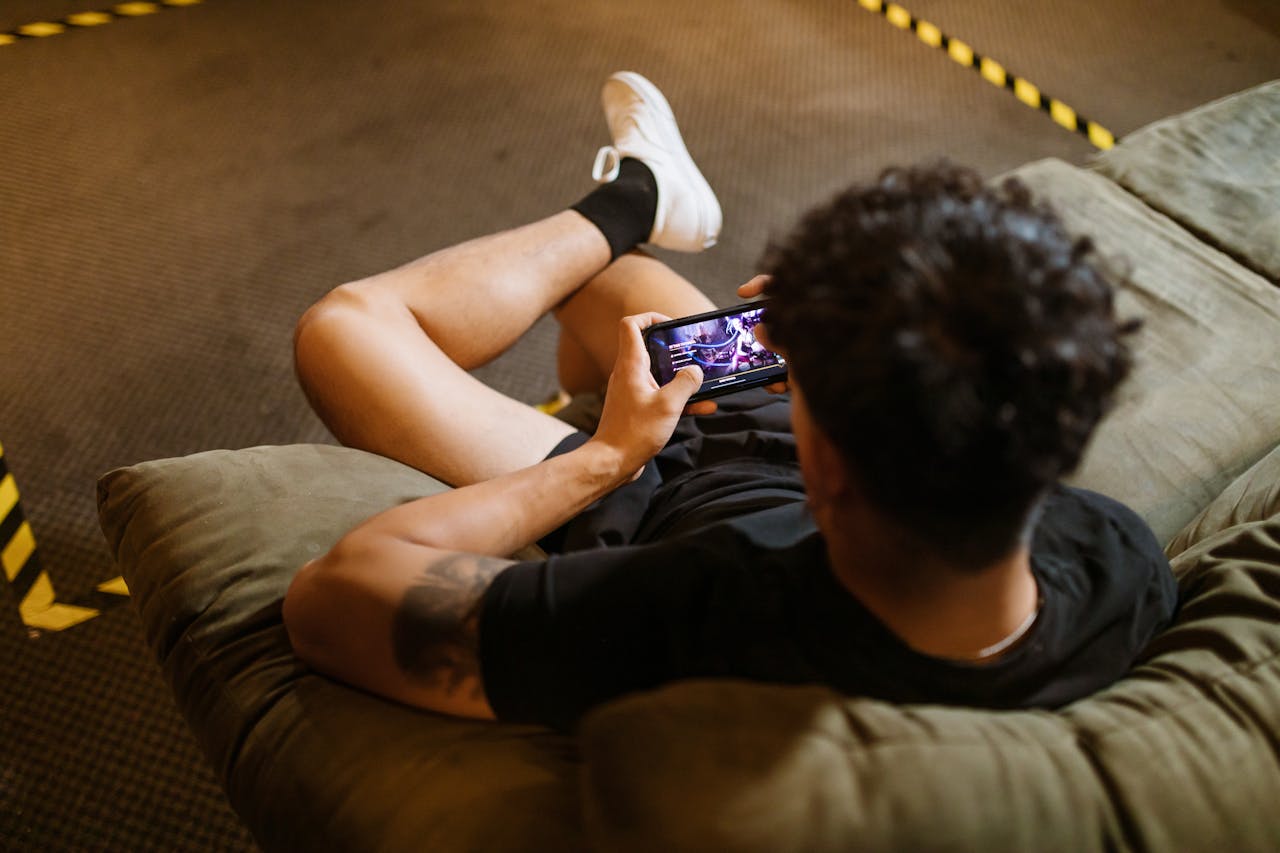 A man relaxing on a sofa playing a video game on his smartphone.